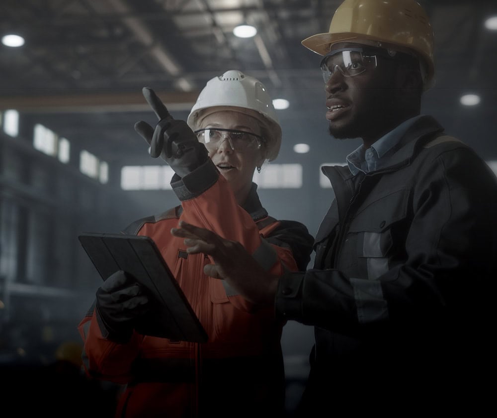 Two industrial workers in safety gear discussing in a factory setting.