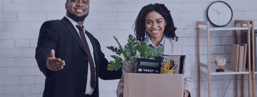 A smiling new employee holding a box of office supplies while being welcomed by a colleague, representing strategies for making a lasting impression in the first 90 days of a new job in 2025.