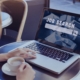 Woman using a laptop with “Job Search” on the screen while holding a coffee cup, symbolizing a mid-year career relaunch through a recruitment agency