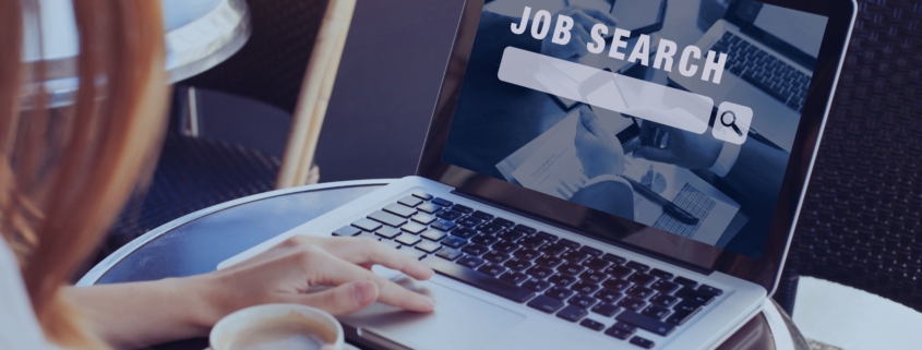 Woman using a laptop with “Job Search” on the screen while holding a coffee cup, symbolizing a mid-year career relaunch through a recruitment agency